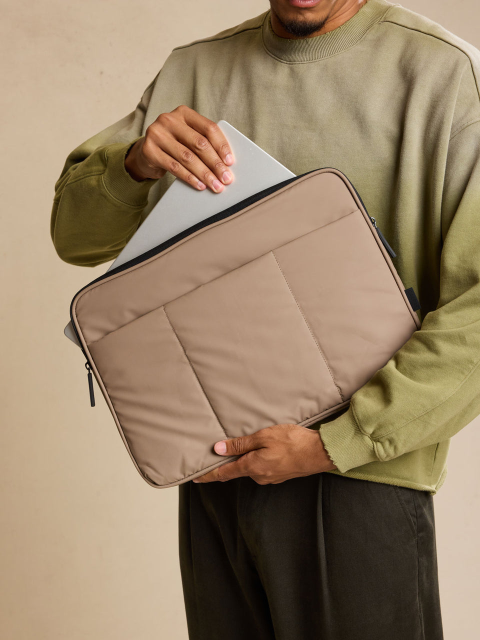 Model putting in laptop into CALPAK Luka Padded Laptop Sleeve in brown Chocolate with puffy exterior; ALD2501-CHOCOLATE