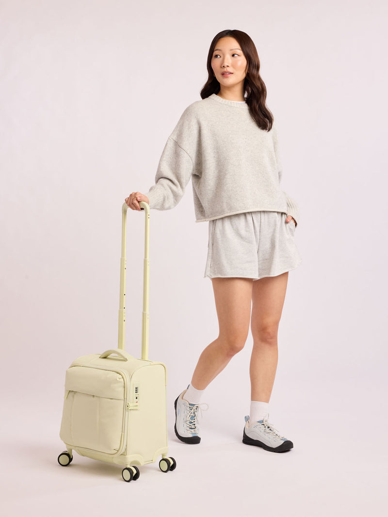 Model with CALPAK Luka Soft-Sided Mini Carry On Luggage in light green Celadon with spinner wheels and handle