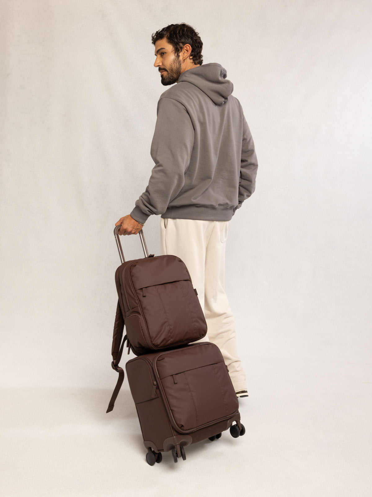 Man holding CALPAK Mini Luka Soft-Sided Carry On Luggage brown Walnut; LSM1014-WALNUT