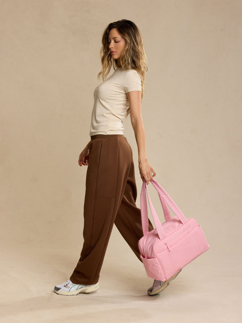 Woman holding CALPAK Luka Mini Duffel in pink Blossom against a beige background