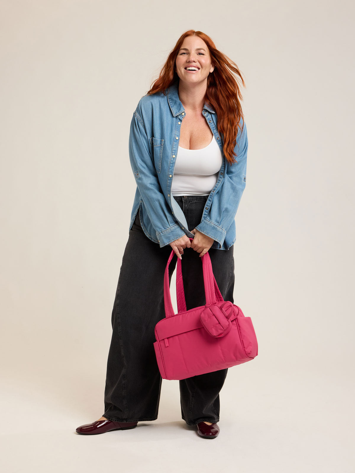 Model holding CALPAK Luka Mini Duffel in bright pink on a white background; DLM2501-DRAGONFRUIT