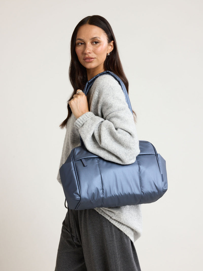 Model wearing the CALPAK Luka Mini Duffel in metallic dark blue Metallic Indigo