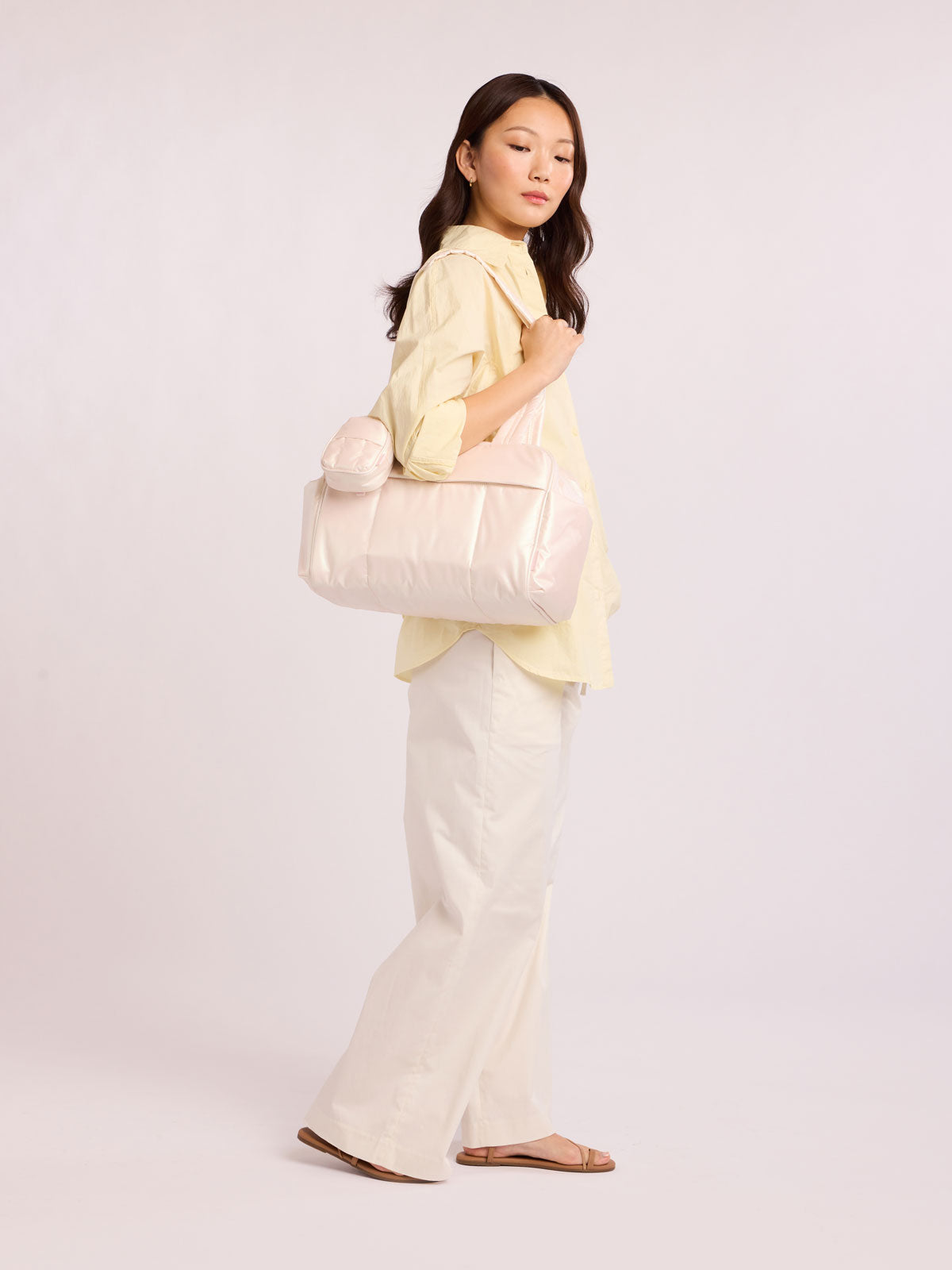 Woman wearing CALPAK Luka Mini Duffel in light pink shiny Pearlescent; DLM2501-PEARLESCENT