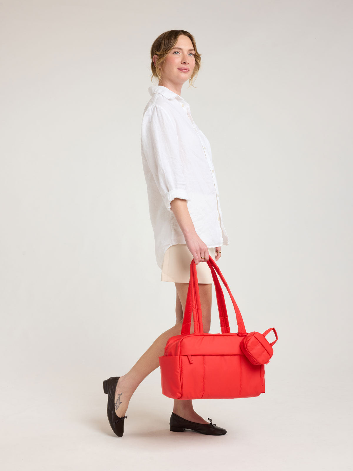 Model holding CALPAK Luka Mini Duffel in red Tomato; DLM2501-TOMATO