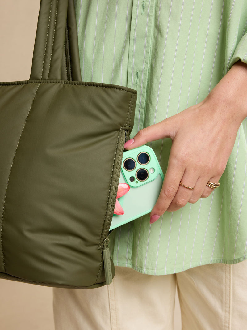 Model putting phone in side pocket of CALPAK Luka Mini Tote in dark green Pine