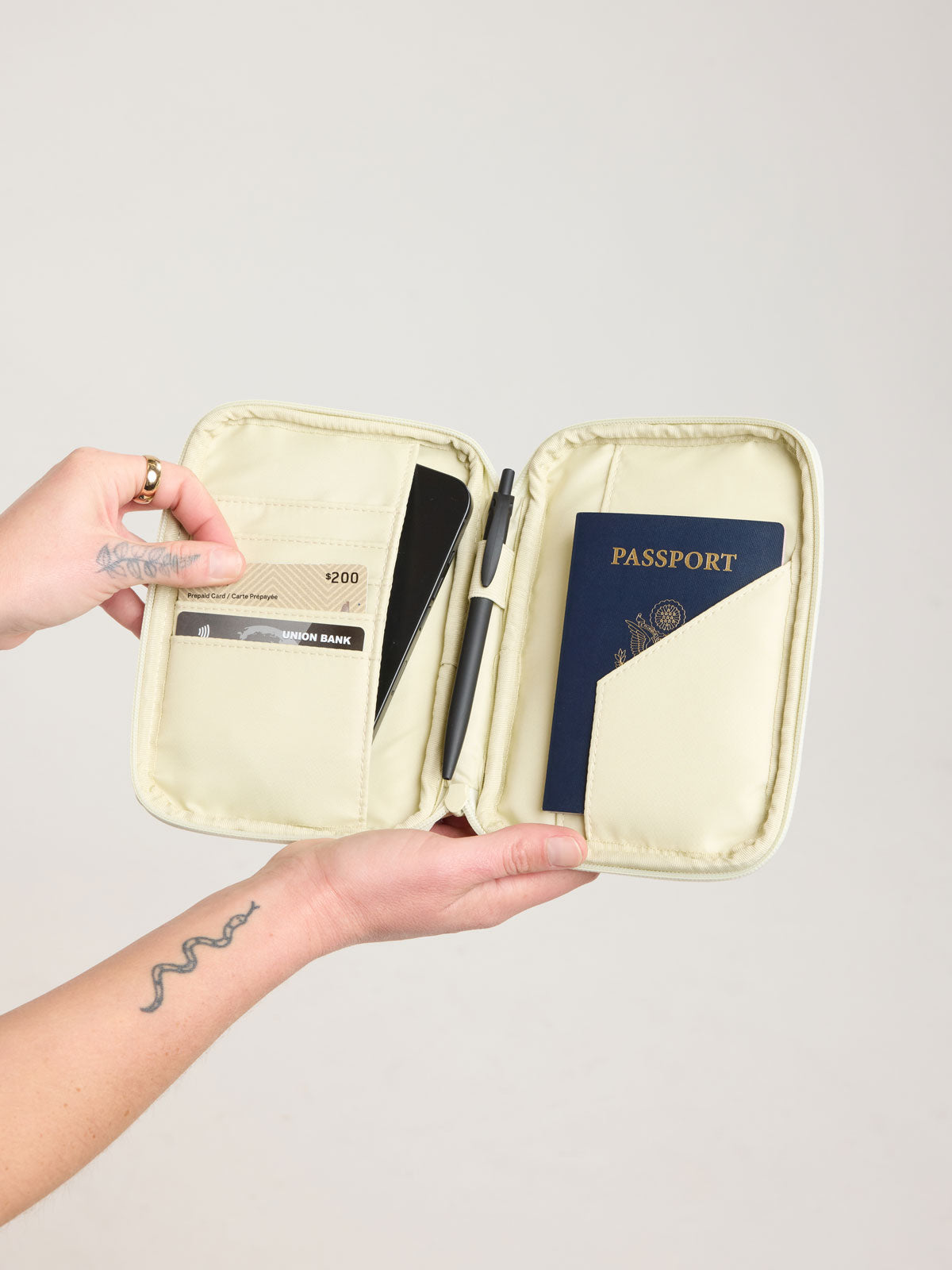 Person holding open CALPAK Luka Zip Passport Wallet in light green Celadon; PZW2301-CELADON
