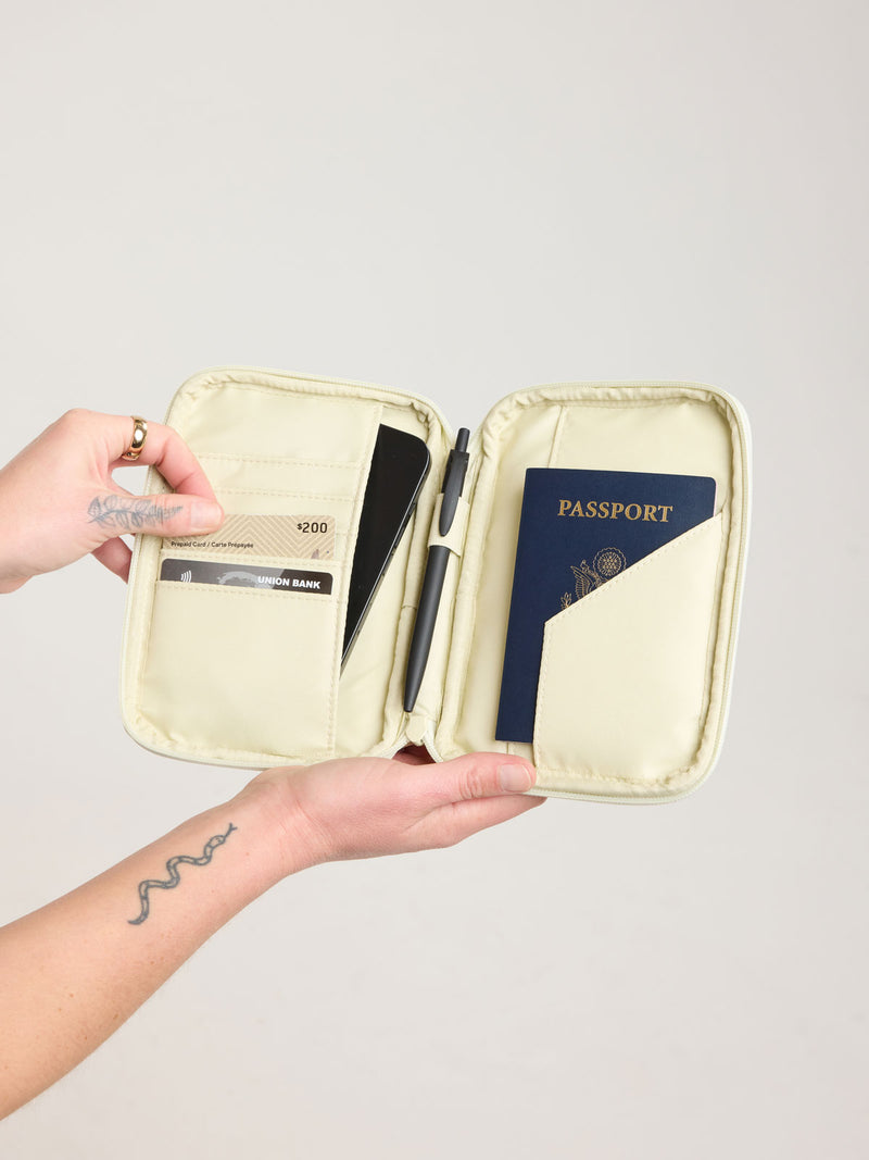 Person holding open CALPAK Luka Zip Passport Wallet in light green Celadon