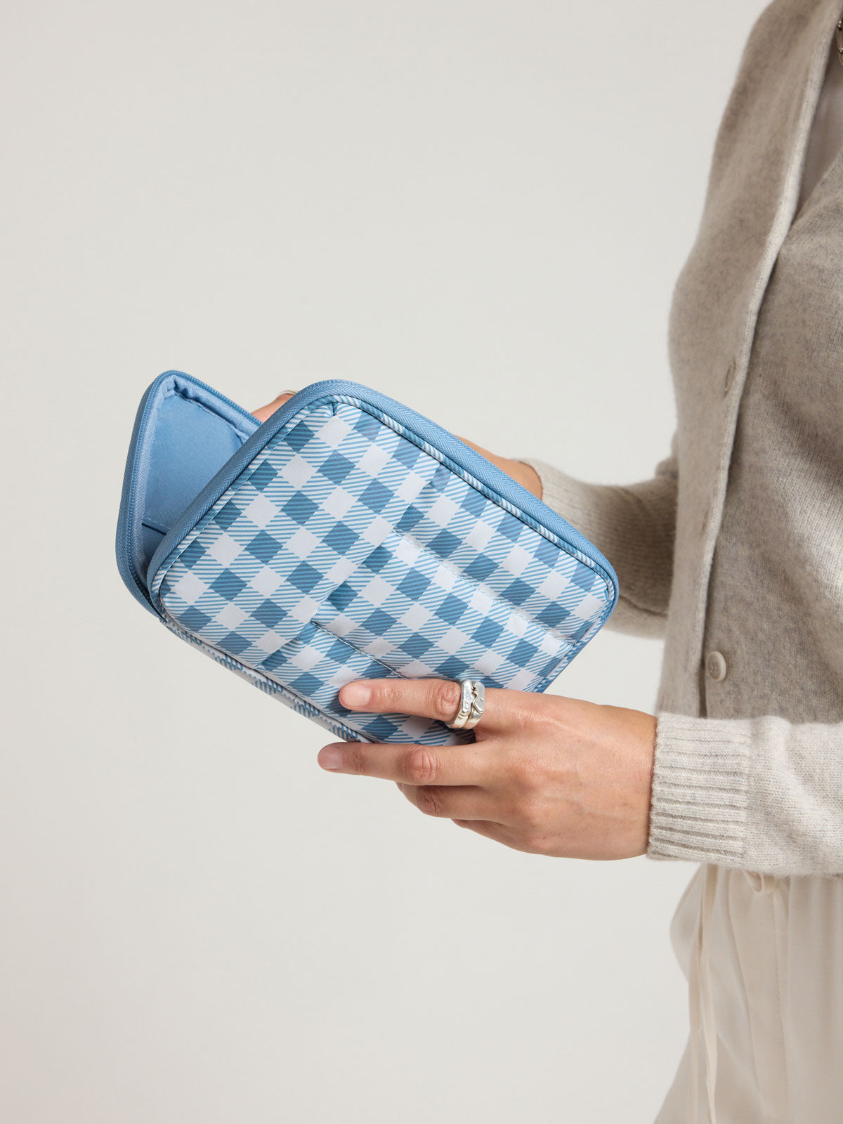 Woman holding the CALPAK Luka Zippered Passport Wallet in white and blue gingham print in French Blue Gingham; PZW2301-FRENCH-BLUE-GINGHAM