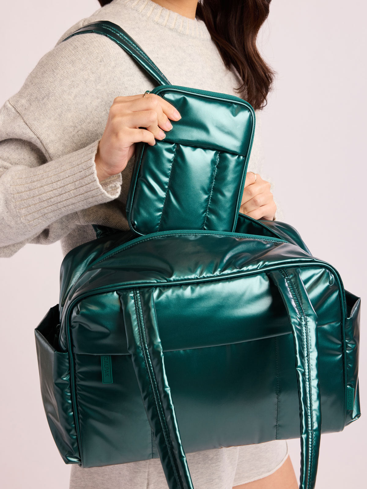 Woman with CALPAK Luka Zip Passport Wallet in dark green shiny Glazed Kale; PZW2301-GLAZED-KALE