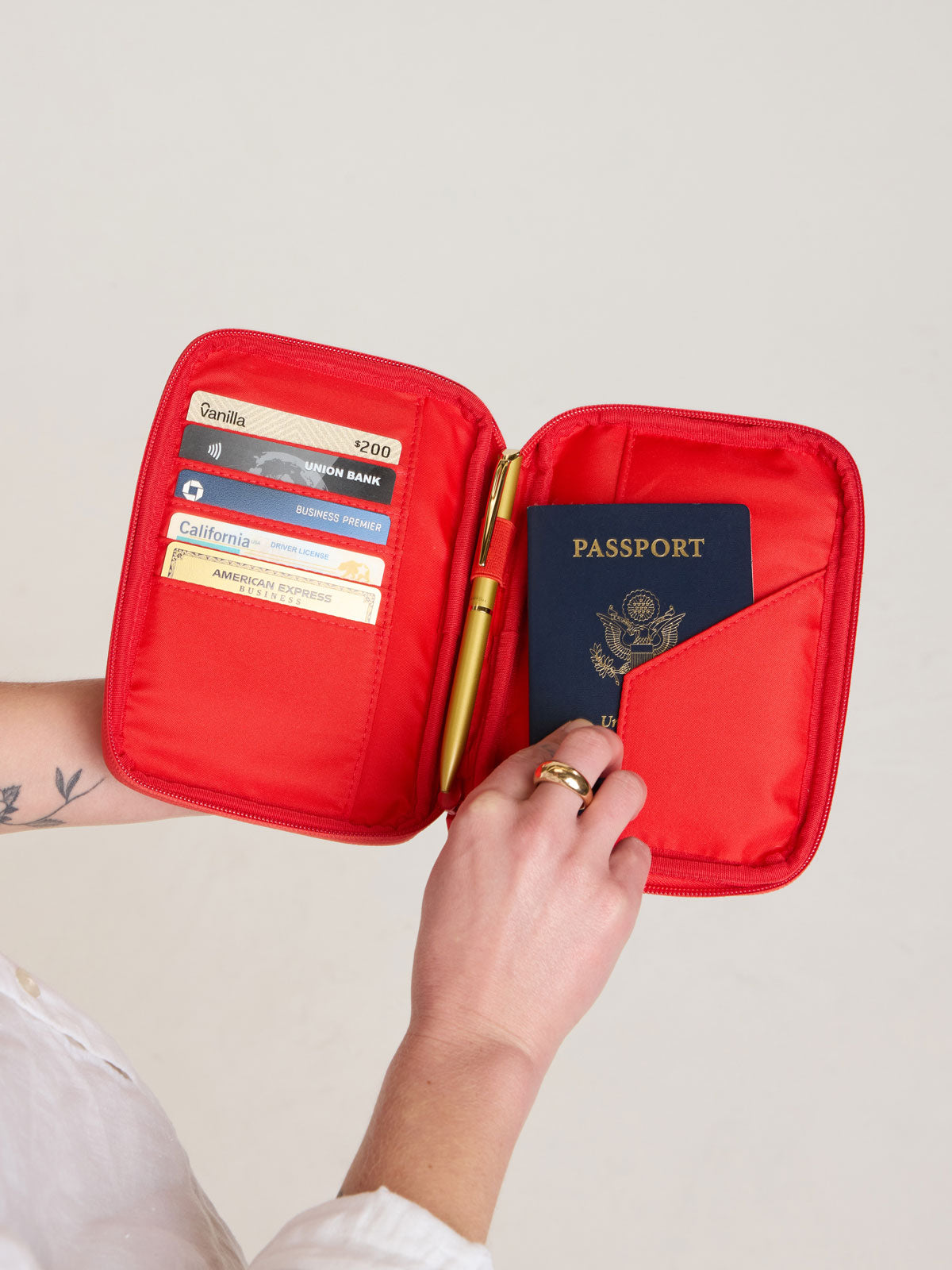 Person holding open CALPAK Luka Zip Passport Wallet in red Tomato; PZW2301-TOMATO
