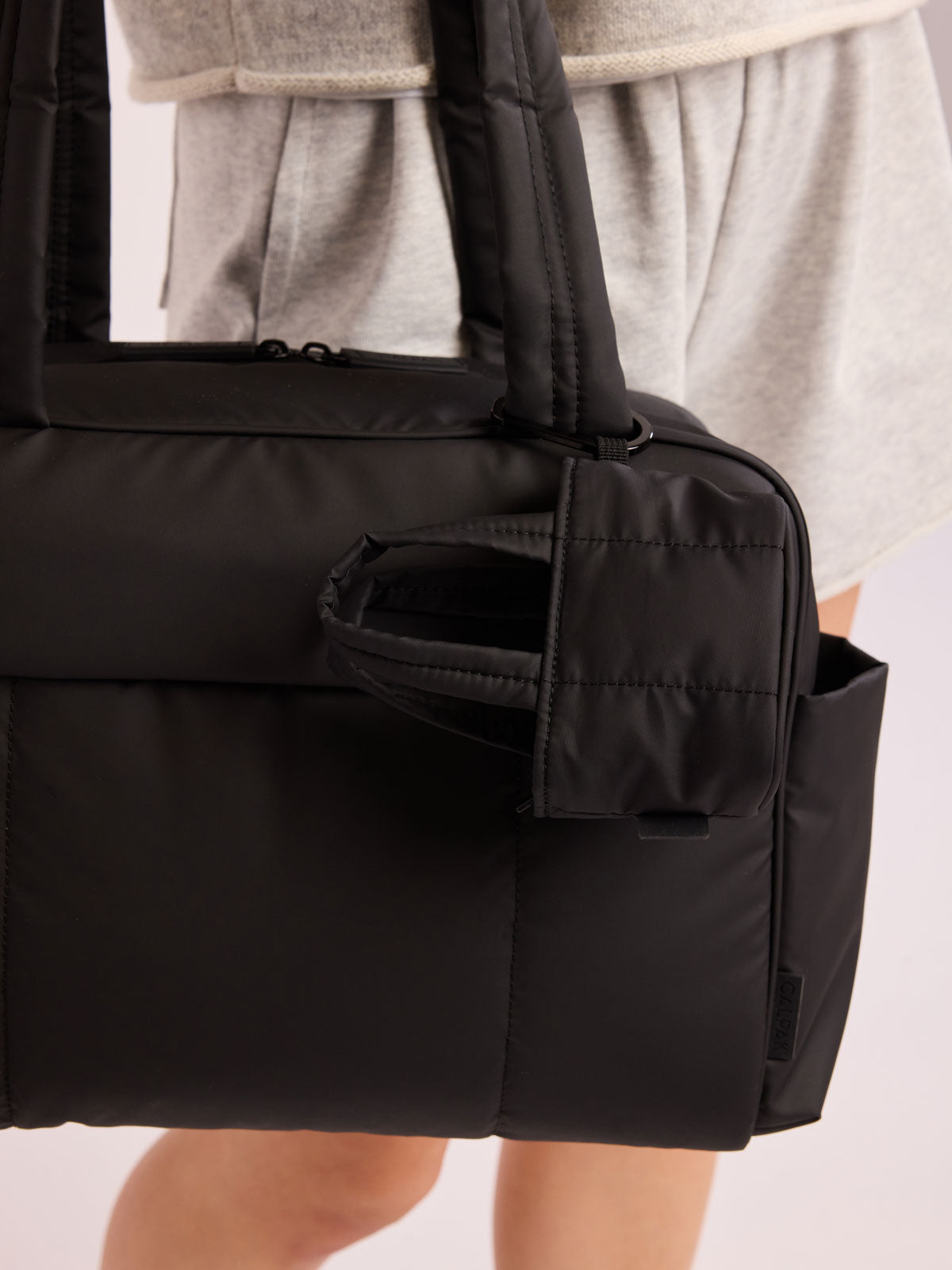 Model holding bag that has the CALPAK Luka Tote Zip Bag Charm in Matte Black with carabiner attached; AMT2601-MATTE-BLACK