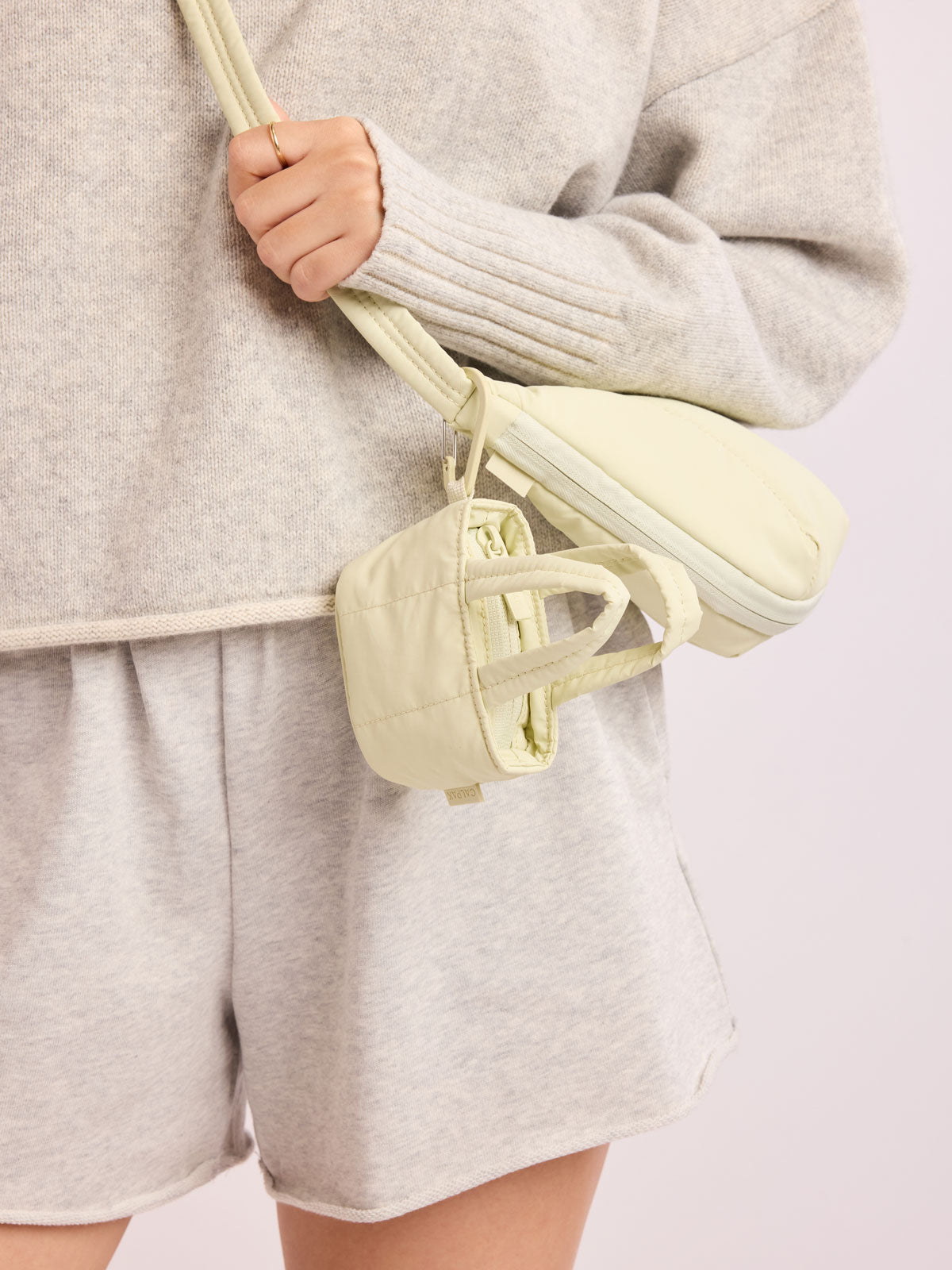 Model with bag that has CALPAK Luka Tote Zip Bag Charm in light green Celadon with carabiner attached; AMT2601-CELADON