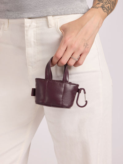 A small deep burgundy Dark Cherry CALPAK Luka Tote Bag Charm with dual top handles and a black carabiner clip attached to the side, shown against a plain white background; AMT2601-DARK-CHERRY-PU view 2