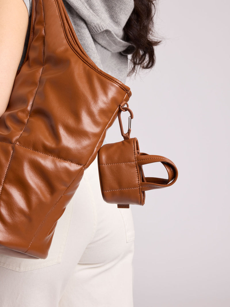 A close-up of a person wearing a large CALPAK Everything Tote in Honey Brown Vegan Leather with a matching small CALPAK Luka Tote Zip Bag Charm attached by a metal ring
