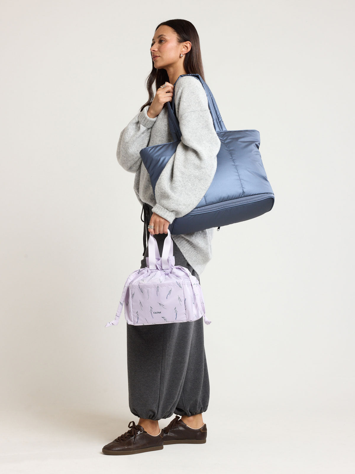 Woman wearing CALPAK Luka Expandable Tote in dark blue metallic material in Metallic Indigo; ALT2201-METALLIC-INDIGO