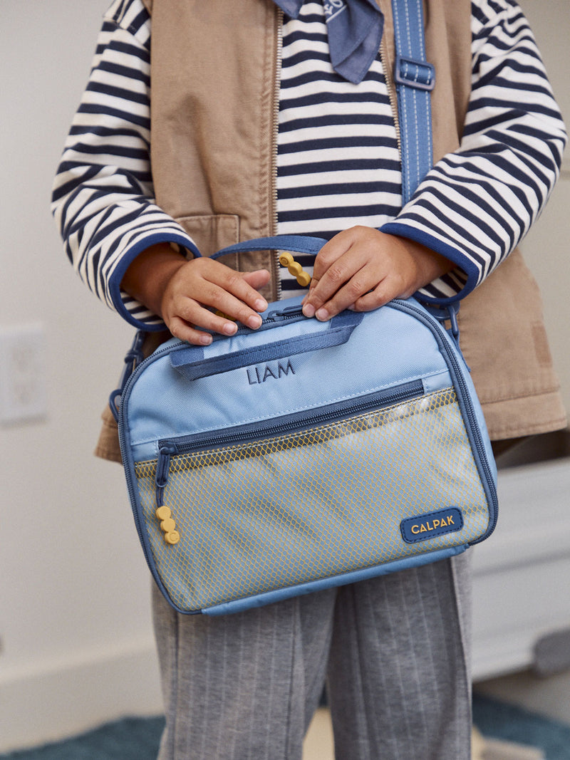 CALPAK Kids Lunch Bag in Blue personalized with name "Liam" being held by child