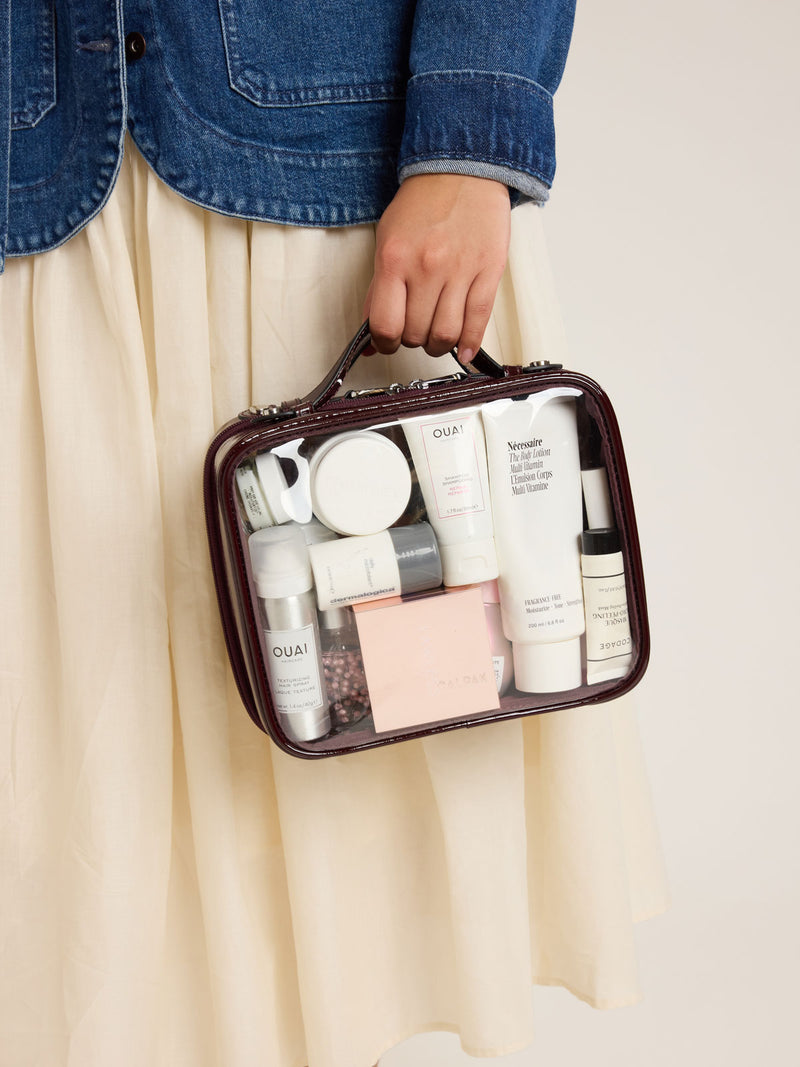 Model holding CALPAK Medium Clear Cosmetic Case in maroon Glazed Dark Cherry on a white background