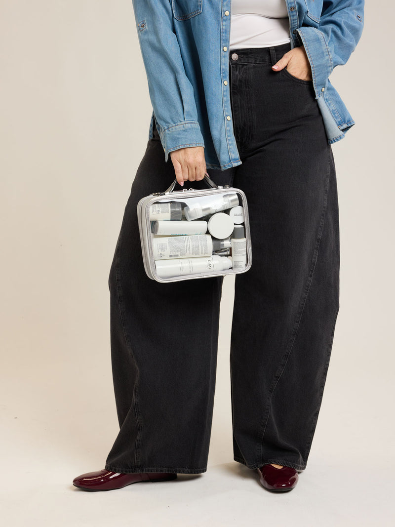 Model holding CALPAK Medium Clear Cosmetic Case in Silver on a white background