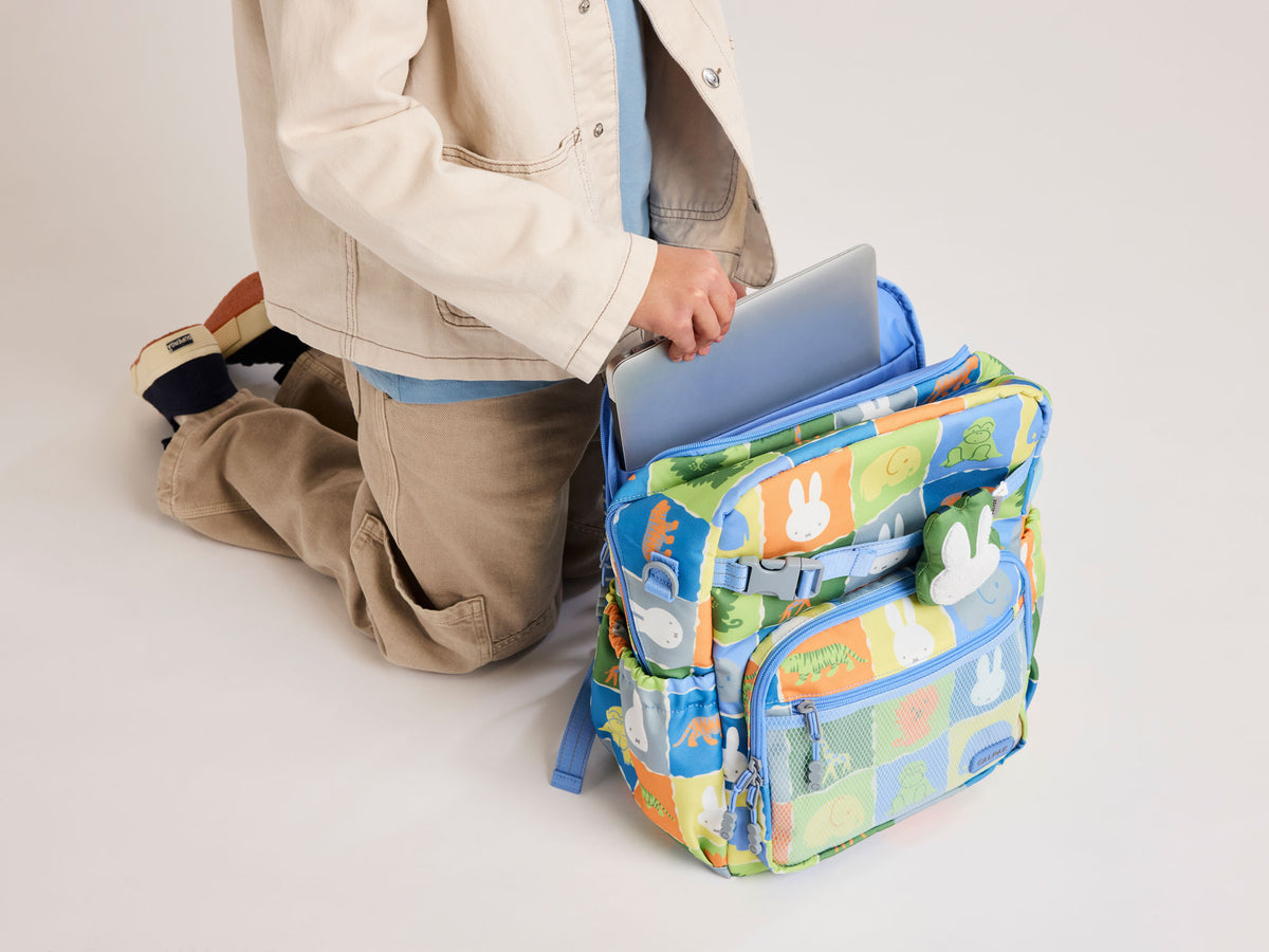 Child model placing laptop inside interior laptop sleeve of blue CALPAK Miffy Kids Backpack
