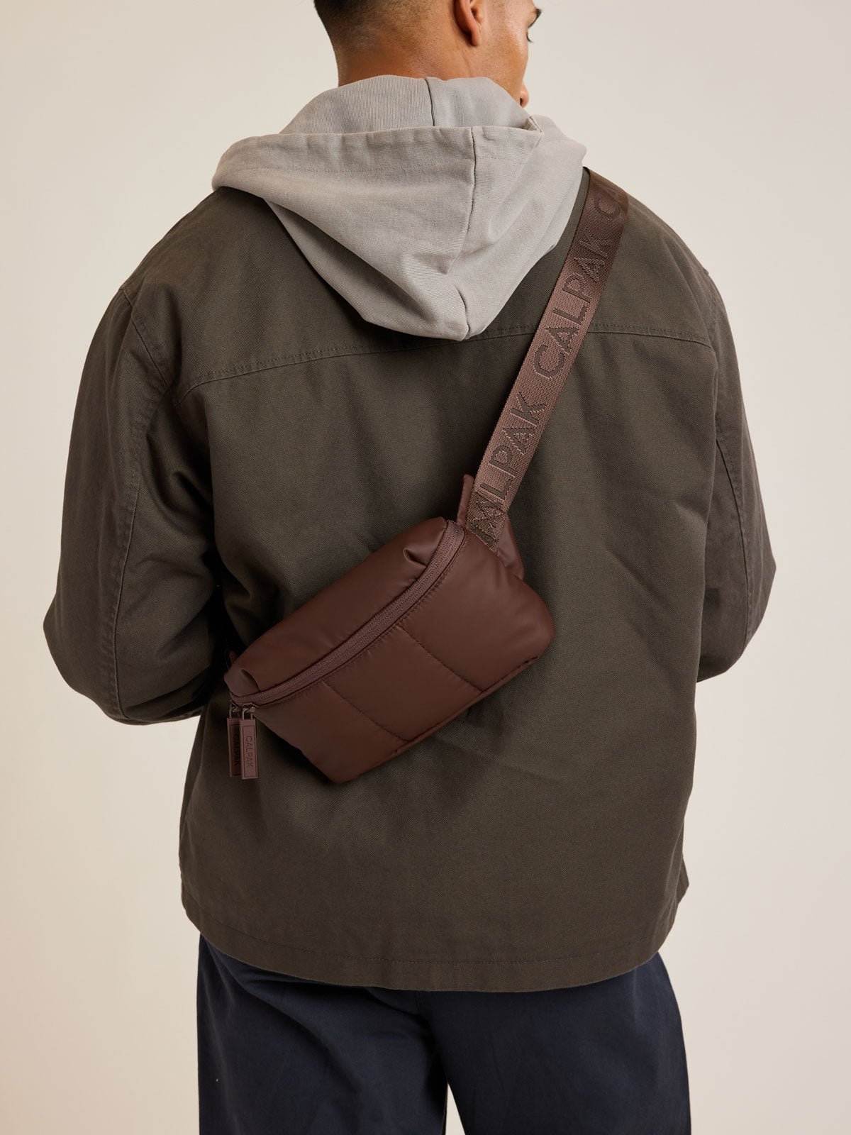 Model wearing CALPAK Luka Mini Belt Bag in brown Walnut on white background; BBM2201-WALNUT