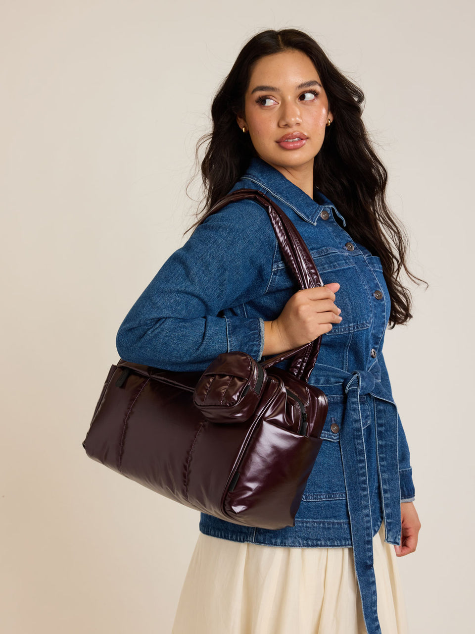 Model wearing the CALPAK Luka Mini Duffel in maroon Glazed Dark Cherry; DLM2501-GLAZED-DARK-CHERRY