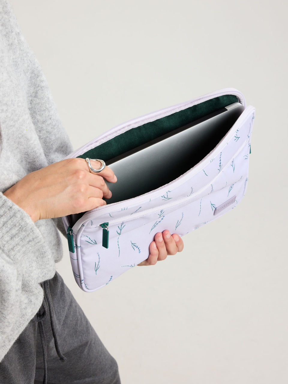 Model putting laptop into the CALPAK Padded Laptop Sleeve 13" in light purple with lavender print Lavender Bloom; ALP2213-LAVENDER-BLOOM
