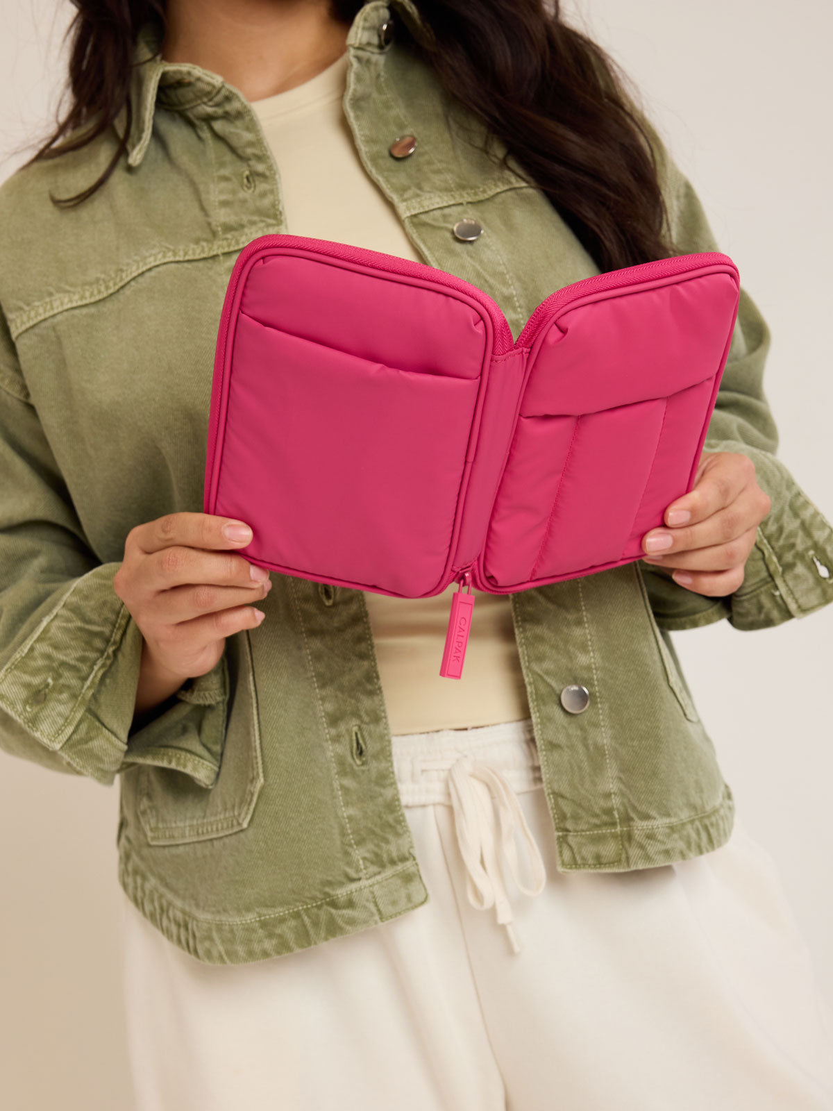 Model holding opened CALPAK Luka Zip Passport Wallet in bright pink Dragonfruit on a white background; PZW2301-DRAGONFRUIT