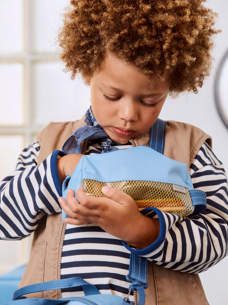 CALPAK Kids Pencil Case in Blue front view with dark blue zippers and yellow mesh front pocket being held by child who is looking into an open pencil case