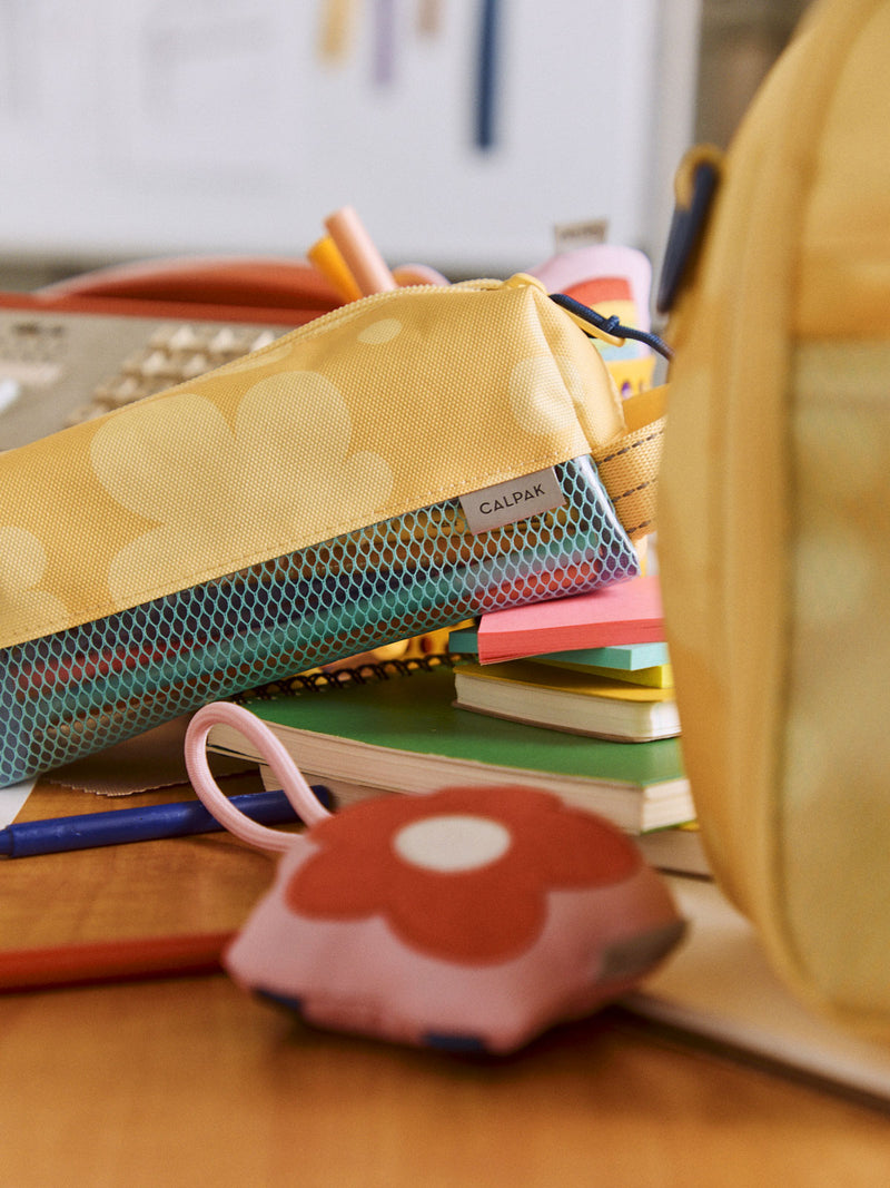 CALPAK Kids Pencil Case in yellow with tan flower print in Yellow Bloom on a student's desk with notebooks and post its; CKPC2501-YELLOW-BLOOM