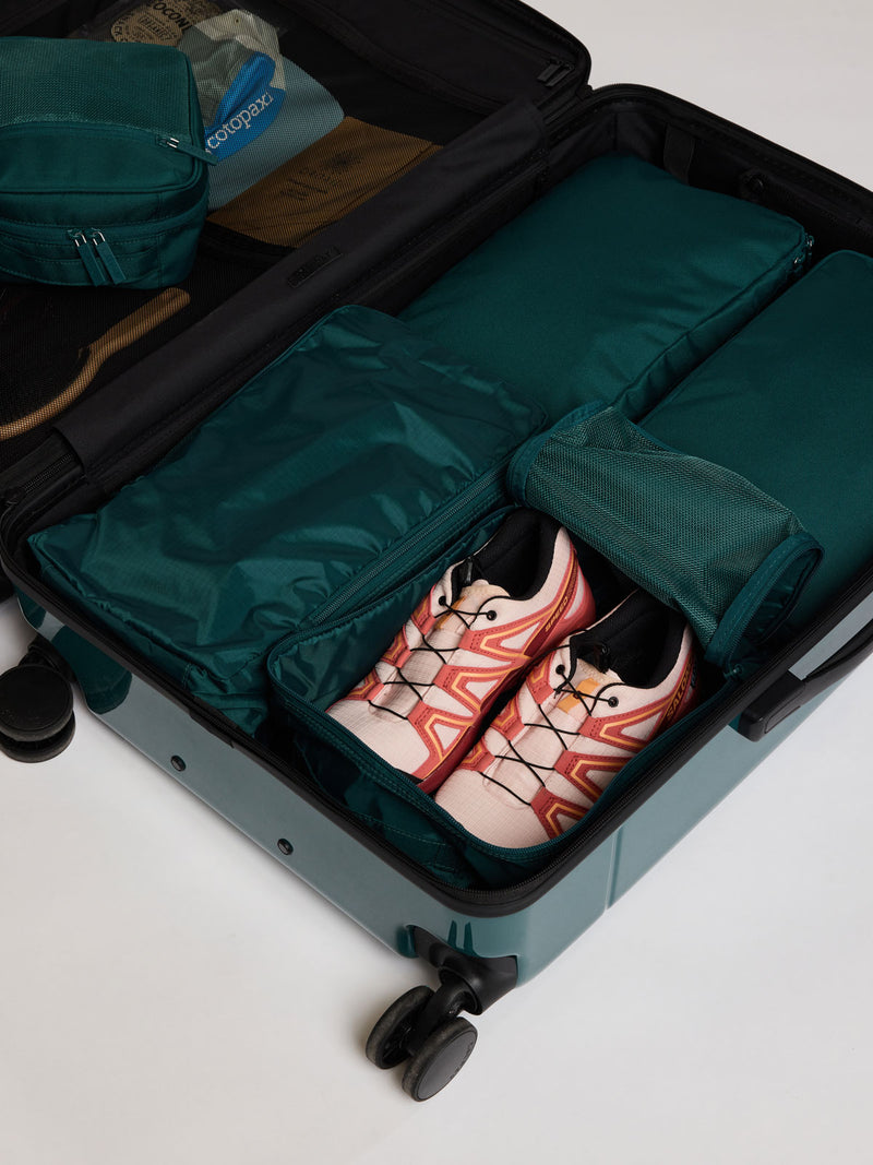 Opened on a white surface, packed with a dark green teal Kale rectangular CALPAK shoe cube with zippers and top handle shown on a plain background