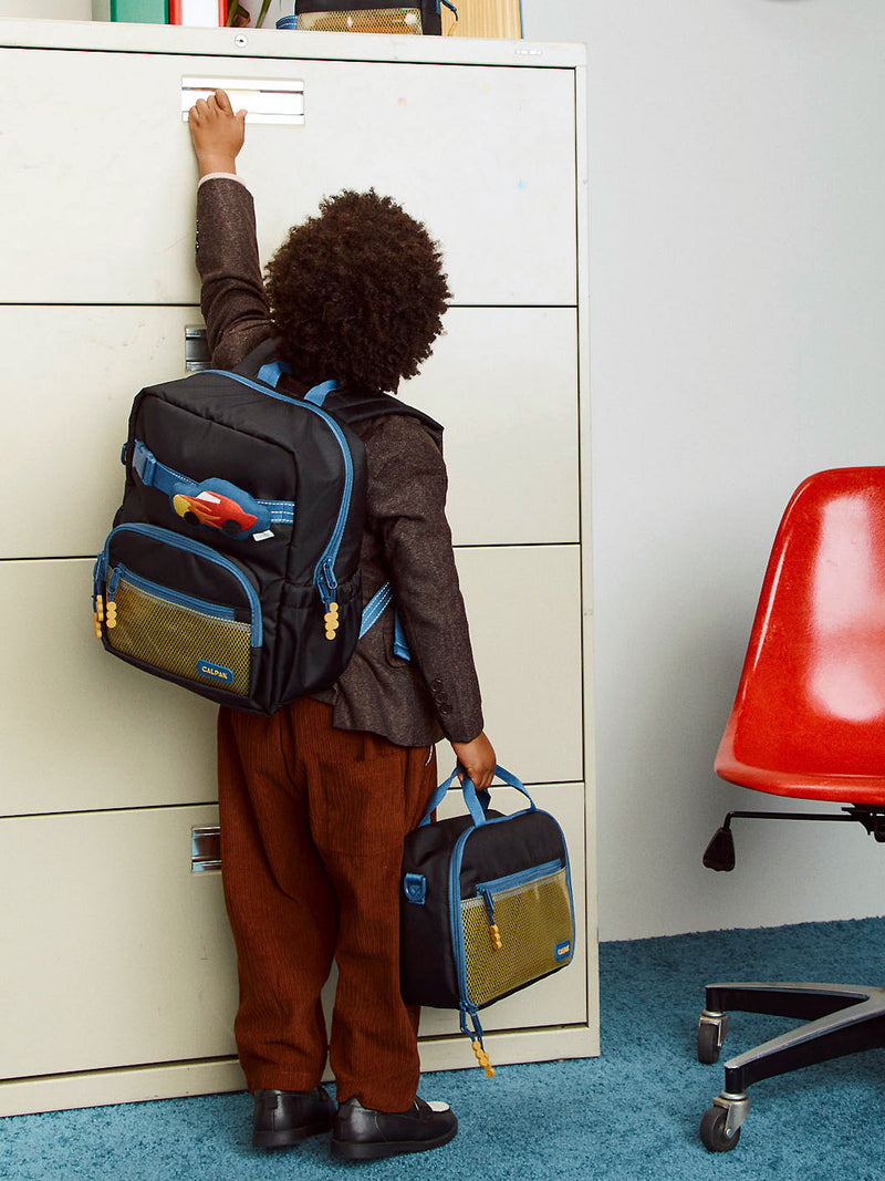 CALPAK Kids Small Backpack in Black for ages 3-5 being worn by child who is opening a school cabinet with CALPAK Kids Lunch Bag in Black in his other hand