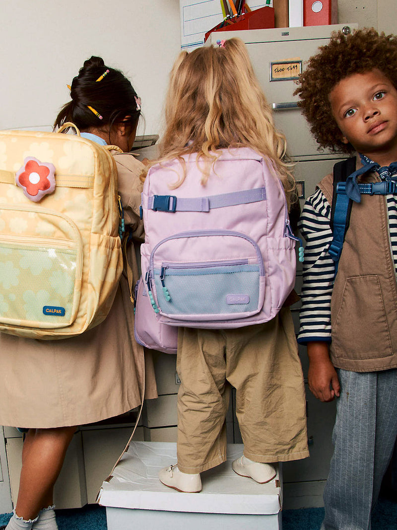 CALPAK Kids Small Backpack in yellow floral Yellow Bloom and pink lavender Orchid Pink being worn by two kids in a classroom