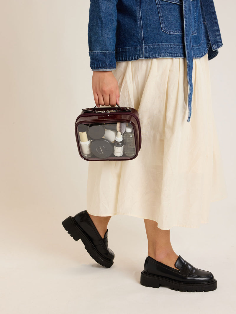Model holding CALPAK Small Clear Cosmetic case in maroon Glazed Dark Cherry