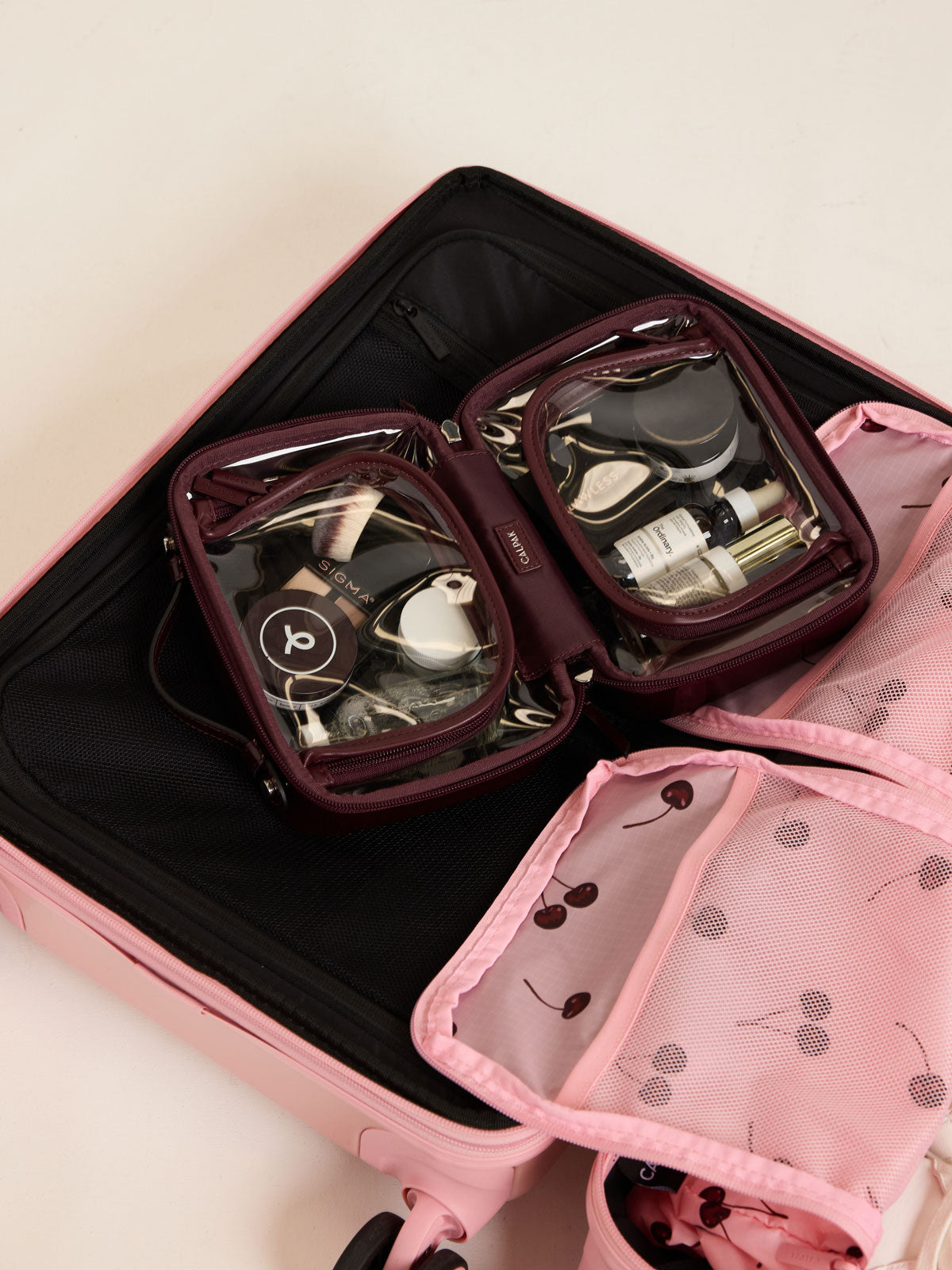 CALPAK Small Clear Cosmetic case in maroon Glazed Dark Cherry in an opened luggage; CCM2001-GLAZED-DARK-CHERRY
