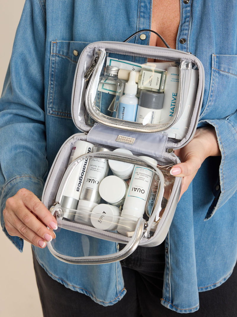 Model holding open CALPAK Small Clear Cosmetic case in Silver