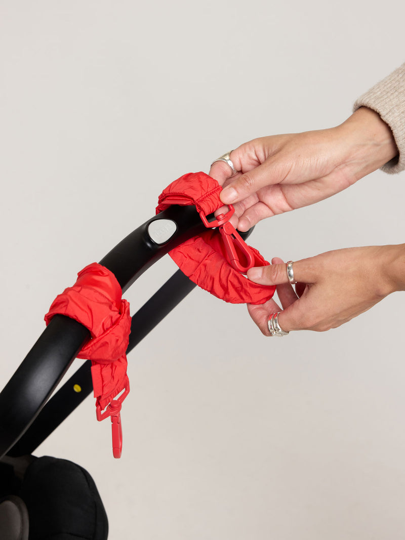 Person adding the CALPAK Stroller Straps in red Tomato to stroller