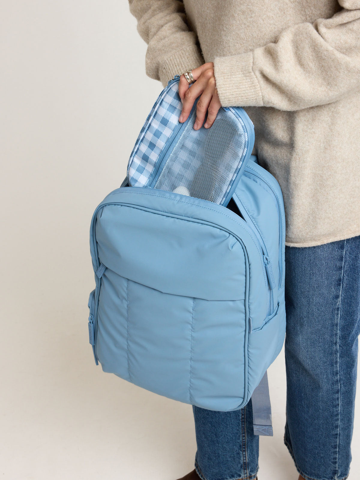 Model putting into a bag the CALPAK Tech Organizer in white and blue gingham pattern in French Blue Gingham; ATC2001-FRENCH-BLUE-GINGHAM