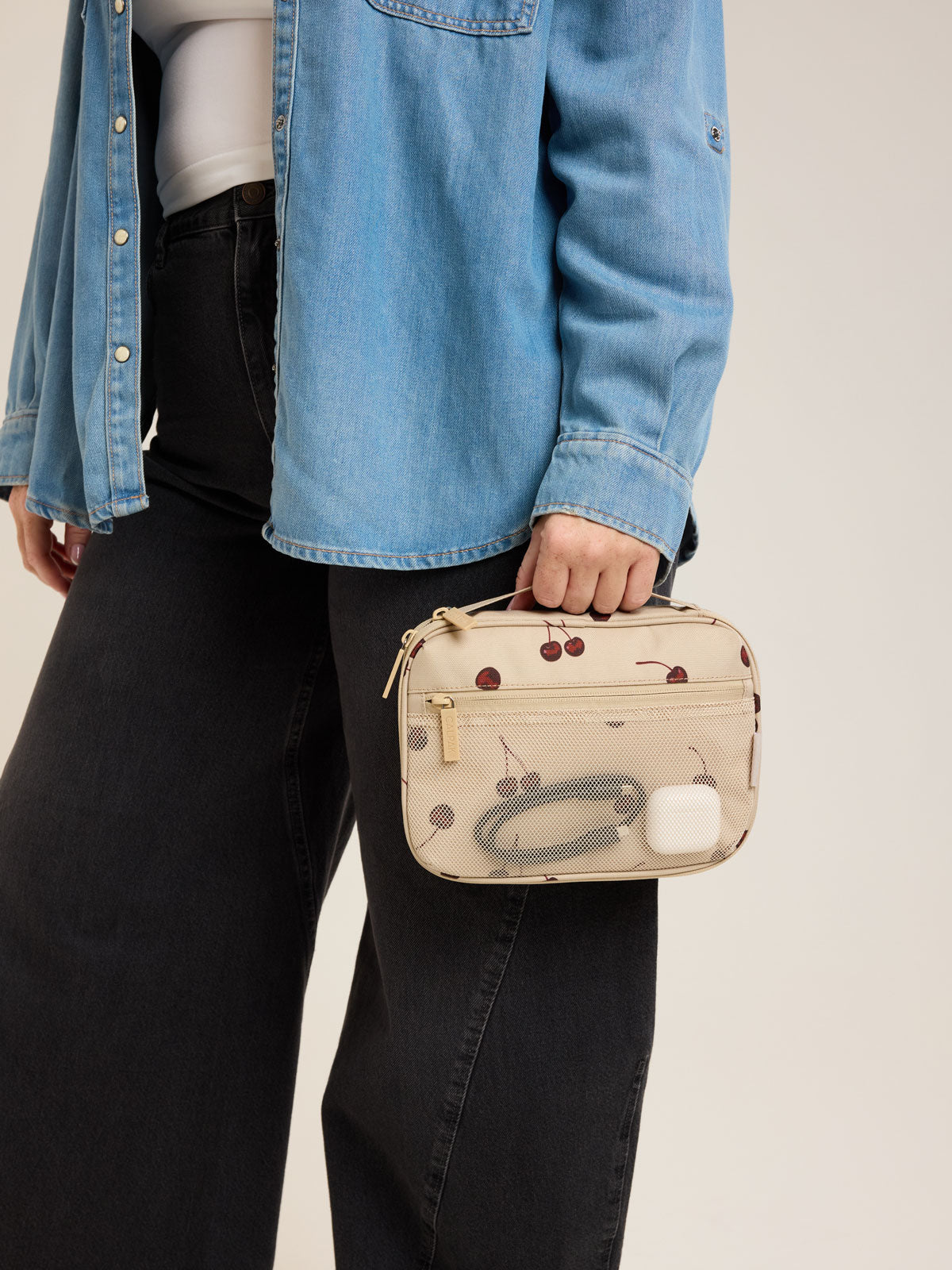 Model holding CALPAK Tech Organizer in beige with cherry print in Oatmeal Blossom; ATC2001-OATMEAL-CHERRY