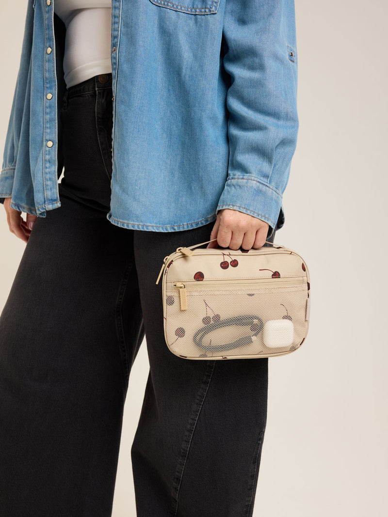 Model holding CALPAK Tech Organizer in beige with cherry print in Oatmeal Blossom