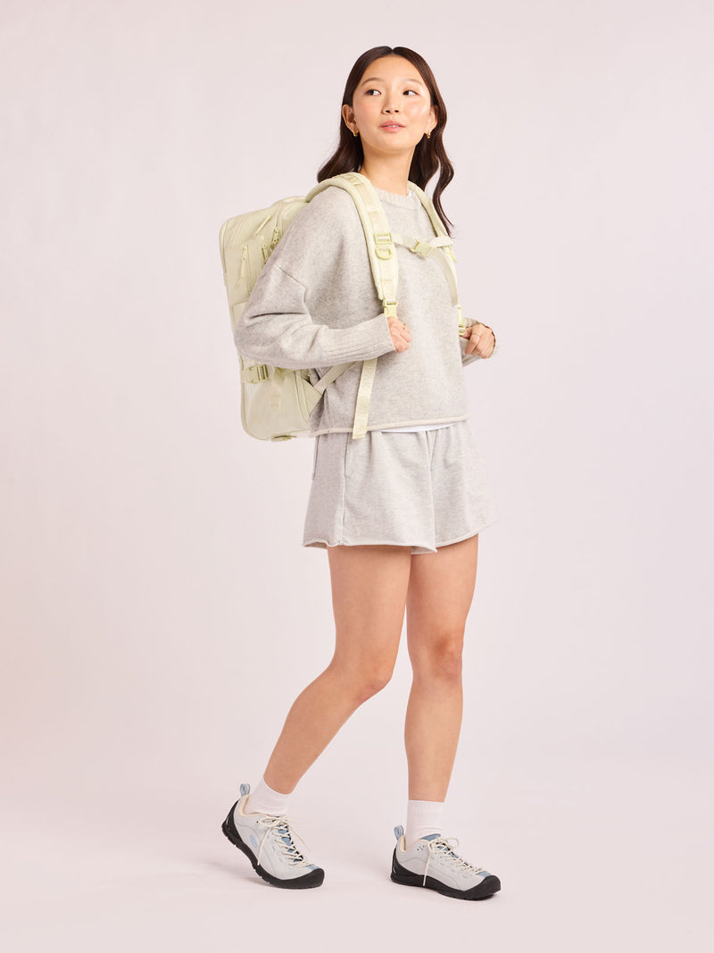 Model wearing the CALPAK Terra 26L Laptop Duffel Backpack with multiple pockets in light green Celadon on a white background
