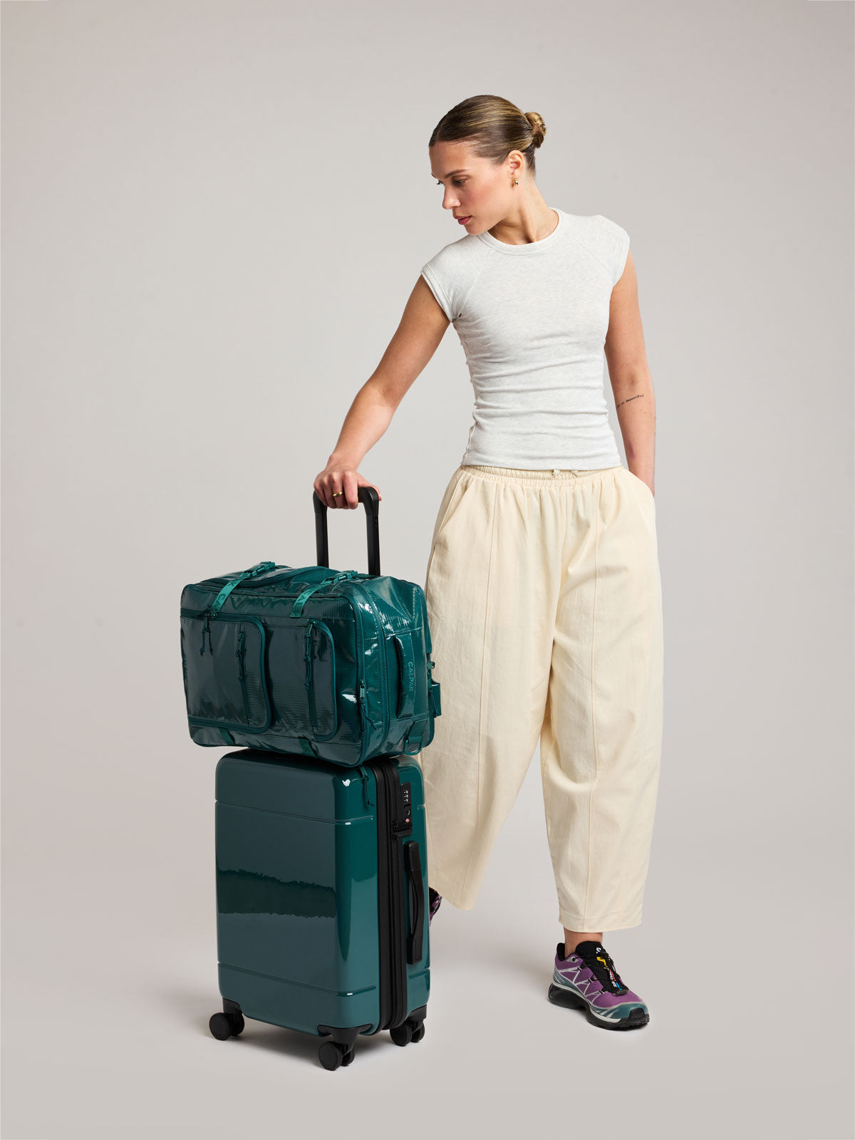 Model with the CALPAK Terra 26L Laptop Backpack in dark blue green Kale with multiple pockets on top of a suitcase; BPH2201-KALE