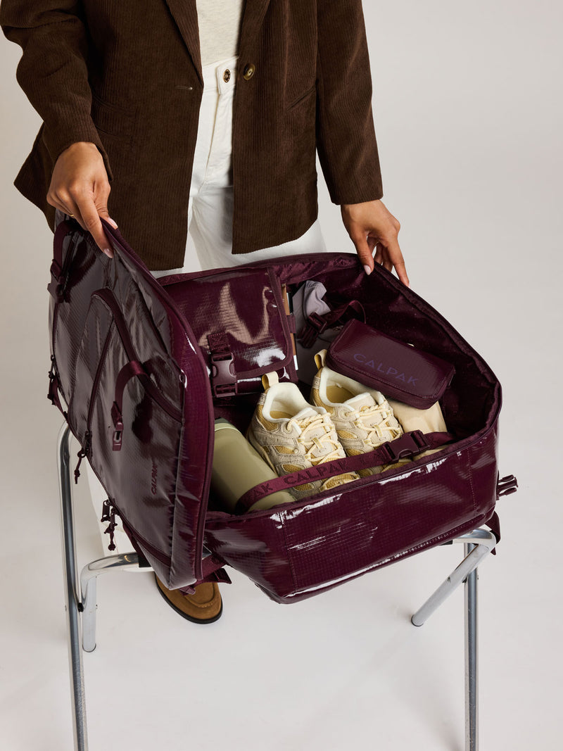 Woman packing shoes in the CALPAK Terra 35L Laptop Backpack Duffel in dark red Dark Cherry with tan accents on a white background