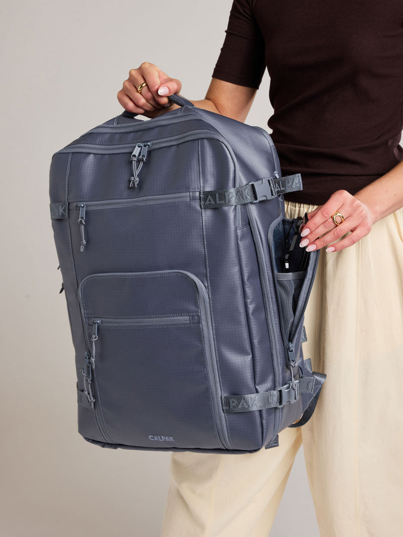 Woman holding the CALPAK Terra 35L Laptop Backpack Duffel in matte dark blue Indigo with tan accents on a white background