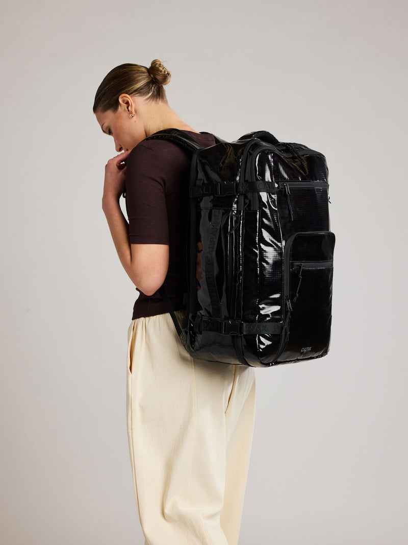 Woman wearing the CALPAK Terra 35L Laptop Duffel Backpack in shiny black Obsidian on a white background