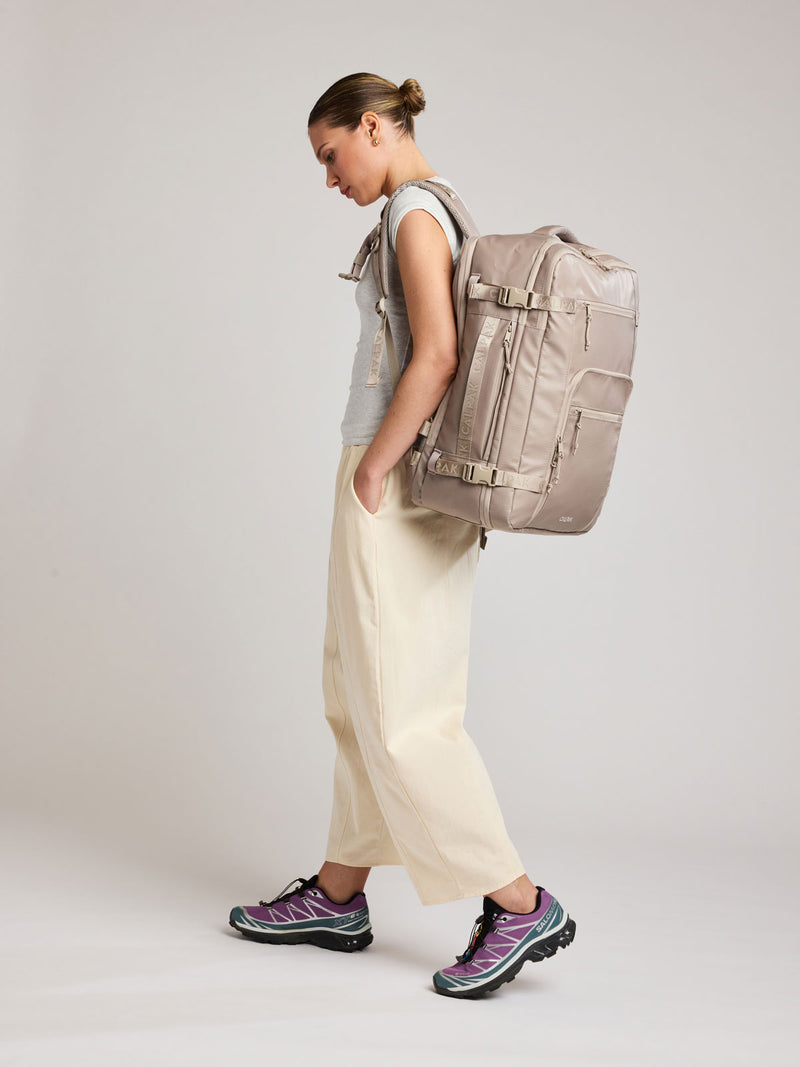 Woman wearing the CALPAK Terra 35L Laptop Backpack Duffel in beige Stone on a white background