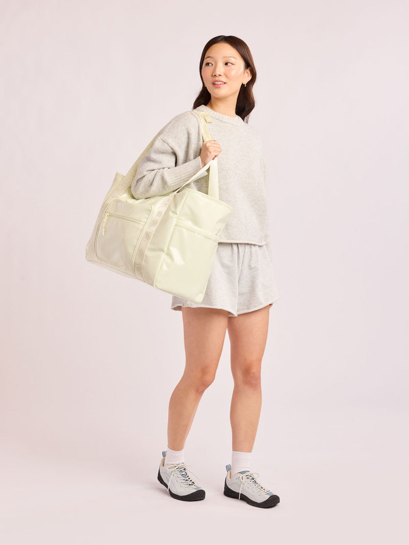 Model wearing beige with the CALPAK Terra 35L Tote Bag with multiple pockets and shoulder straps in shiny light green Celadon on a white background