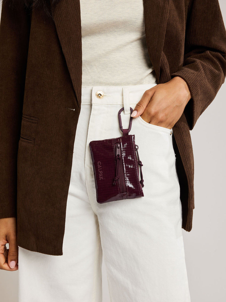 Person with the Dark red Dark Cherry CALPAK Terra Clippable Card Pouch with carabiner clipped on their pant buckle; TPC2401-DARK-CHERRY