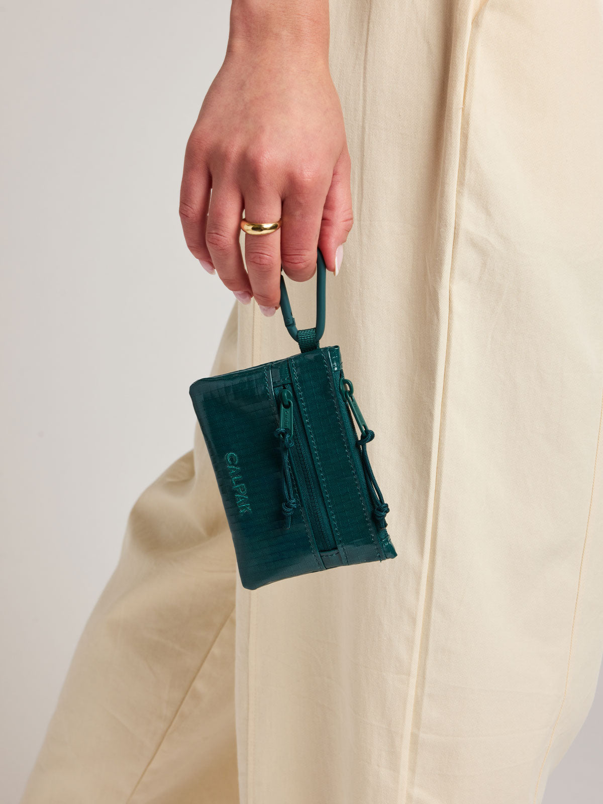 Person with a ring holding the Kale blue green of CALPAK Terra Clippable Card Pouch by the carabiner clip; TPC2401-KALE