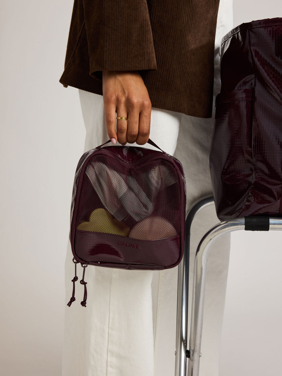 Woman holding the CALPAK Terra 5pc Packing Cube Set in dark red Dark Cherry on a white background; PCT2601-DARK-CHERRY