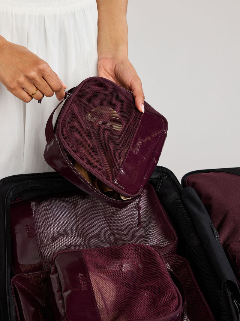 Person packing in a suitcase the CALPAK Terra 5pc Packing Cube Set in dark red Dark Cherry on a white background